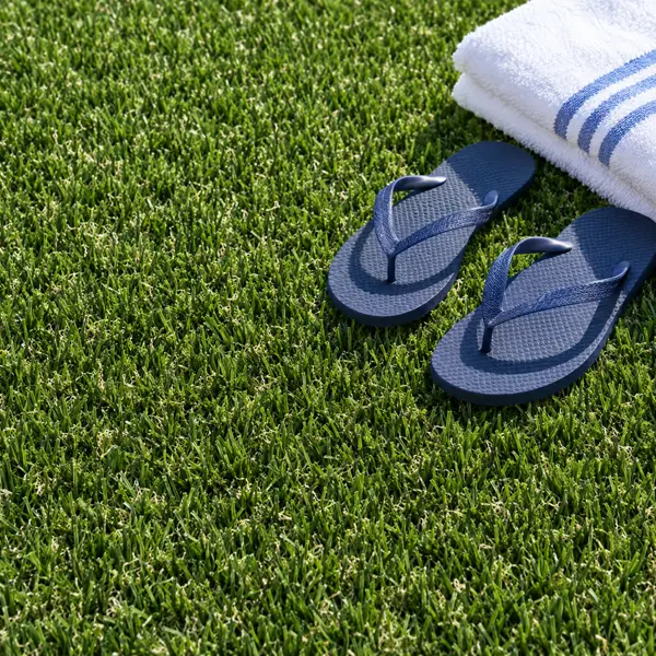 Tongs et serviette posées sur un gazon synthétique en plein soleil